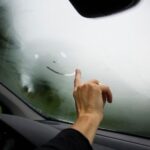 Hand wiping moisture from a fogged car windshield