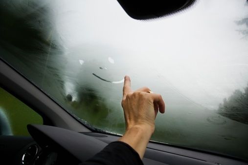 Hand wiping moisture from a fogged car windshield