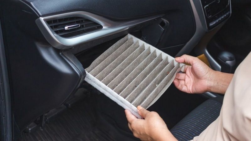 Person removes a pleated cabin air filter from a car dashboard
