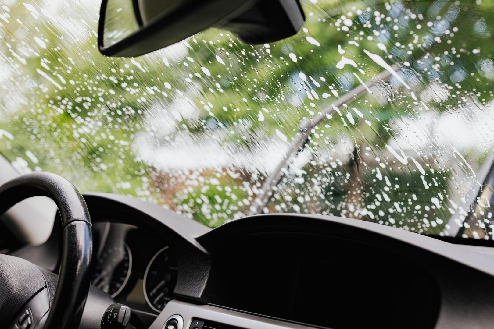 Car dashboard and steering wheel seen through a rain-speckled windshield